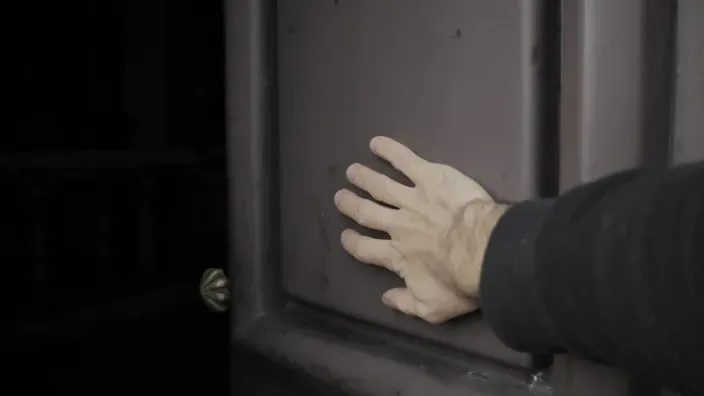 Mano sobre una puerta oscura para representar el riesgo de ocupación en casa y la importancia del seguro de hogar.