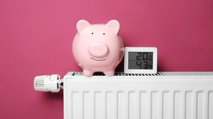 Hucha cerdito rosa y termómetro digital sobre radiador simbolizando ahorro en calefacción.