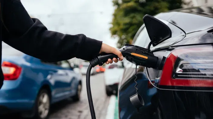 Conductor conectando un coche eléctrico a un cargador en la calle