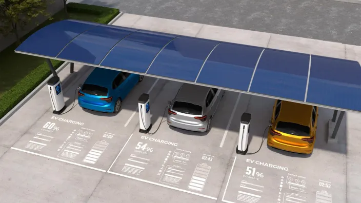 Coches eléctricos cargando en estacionamiento con marquesina solar y datos de carga proyectados en el suelo.