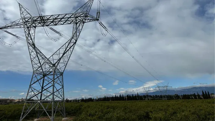 Torre de alta tensión en una zona rural bajo un cielo parcialmente nublado.