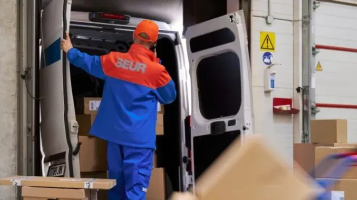 Trabajador de SEUR cargando paquetes en una furgoneta de reparto en un centro logístico.