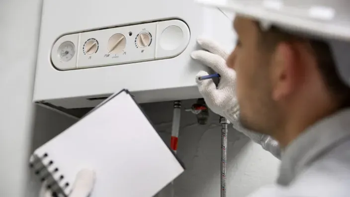 Técnico revisando y anotando datos durante la inspección de una caldera de gas en una vivienda.