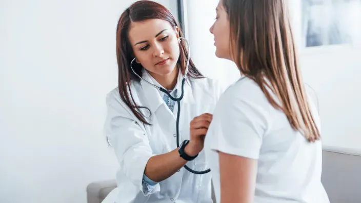 Doctora joven auscultando el pecho de una paciente con estetoscopio durante una consulta médica.