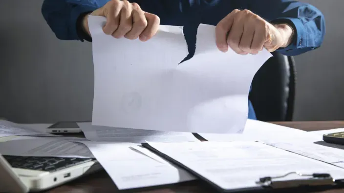 Manos rompiendo un contrato o documento oficial, simbolizando la cancelación de un seguro o servicio.