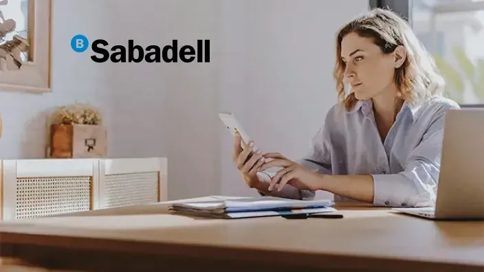 Mujer usando calculadora y portátil para gestionar sus finanzas personales con Banco Sabadell desde casa.