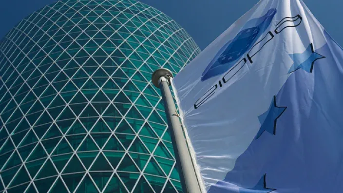 Bandera de la EIOPA frente a un moderno edificio de cristal, simbolizando la regulación de seguros y pensiones.