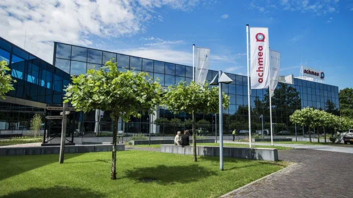 Fachada de cristal del edificio de oficinas de la entidad bancaria Achmea con banderas en la entrada.