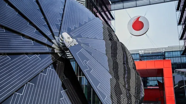 Estructura artística de paneles solares frente a la sede de Vodafone con su logotipo suspendido.