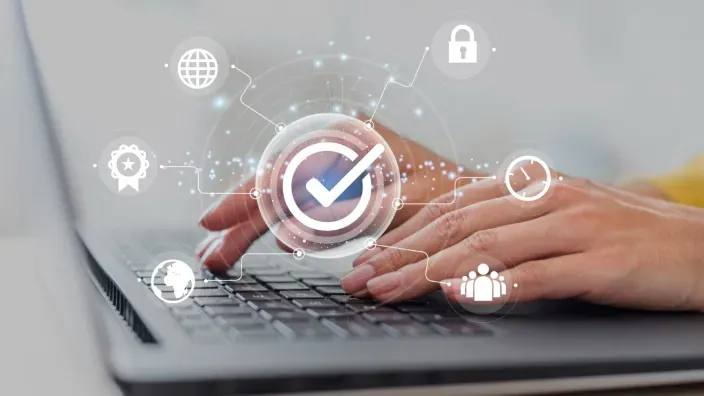 Manos en un portátil con un icono de verificación y estándares de seguridad.