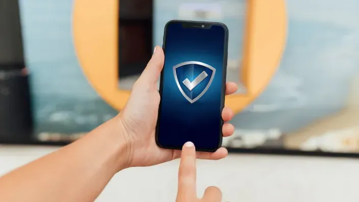Mano sosteniendo un smartphone con un escudo de seguridad verificado en pantalla para protección móvil.