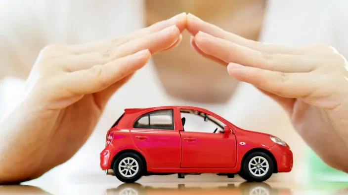 Manos protegiendo un coche rojo de juguete simbolizando el seguro de automóvil o accidentes.