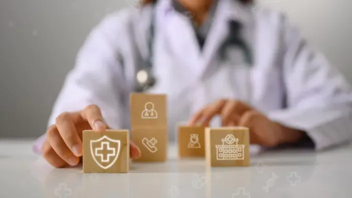 Sanitario colocando cubos de madera con iconos médicos para representar la protección y coberturas de un seguro de salud.