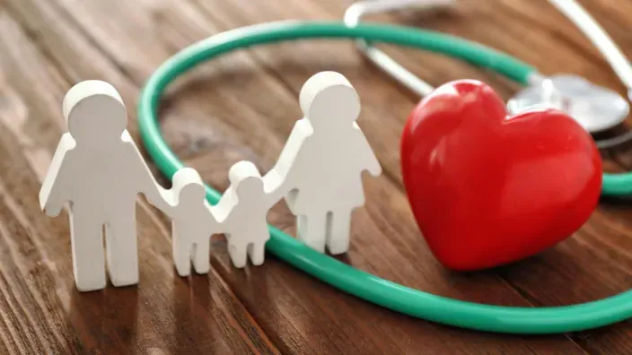 Figura de familia y corazón rojo junto a un estetoscopio sobre una mesa de madera, simbolizando protección y seguros de salud.
