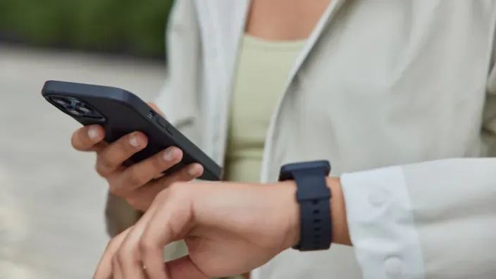 Persona consultando su smartwatch y smartphone para representar la conectividad total y el uso de dispositivos móviles.