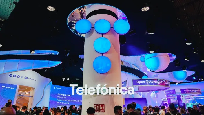 Stand de Telefónica en un evento tecnológico con iluminación azul y pantallas sobre innovación en 5G y conectividad.