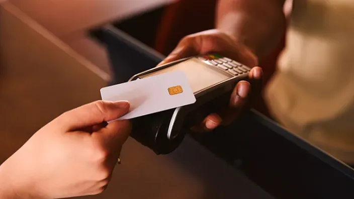 Tarjeta bancaria acercándose a un terminal de pago sostenido por otra persona