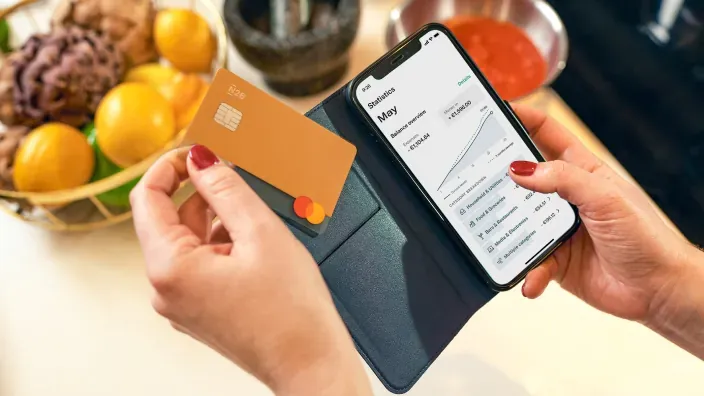 Persona utilizando la aplicación de N26 en el móvil mientras sostiene una tarjeta bancaria en una cartera.