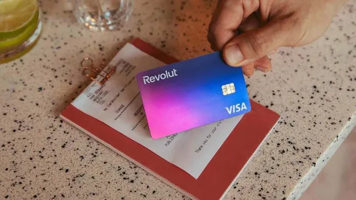 Persona sostiene una tarjeta Revolut Visa sobre una cuenta en la mesa de un restaurante.