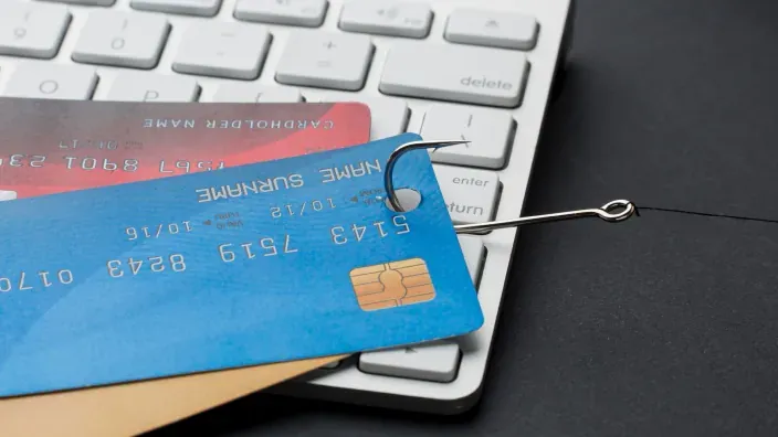 Tarjetas bancarias enganchadas con un anzuelo sobre un teclado de ordenador, concepto de fraude o phishing financiero.