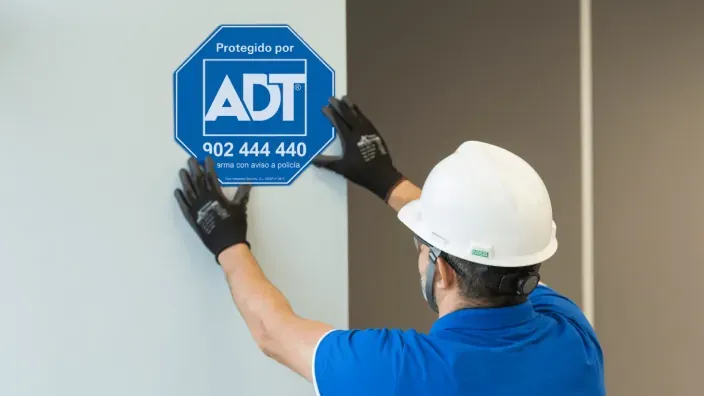 Técnico de ADT instalando un cartel de alarma en una pared interior.