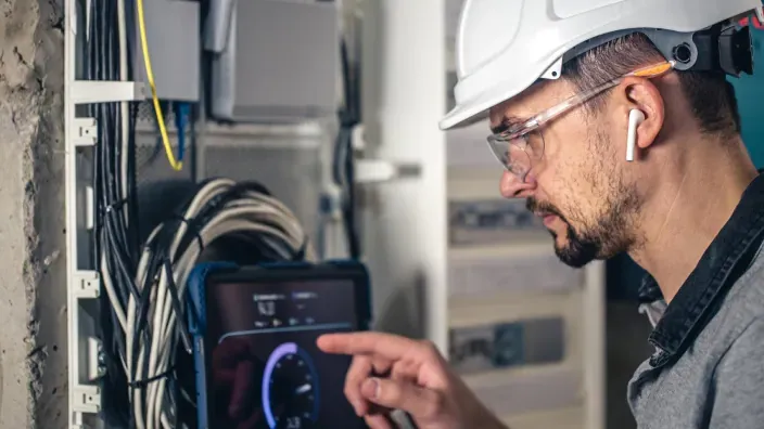 Técnico de redes usando una tablet para el mantenimiento de fibra óptica e internet de alta velocidad en una instalación.