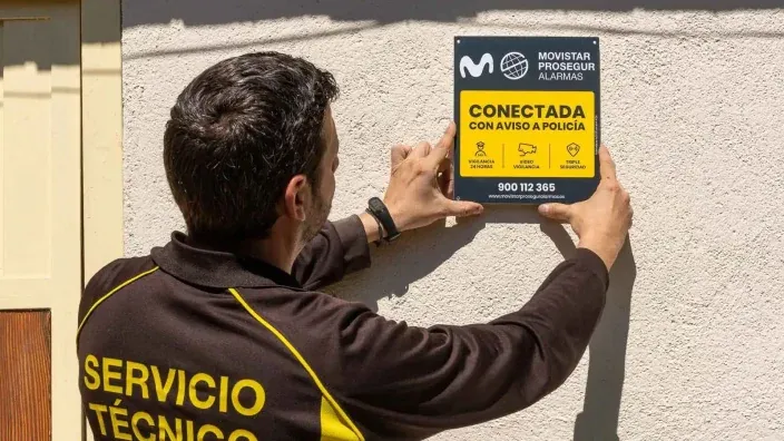 Técnico de Movistar Prosegur Alarmas instalando el cartel disuasorio de Conectada con aviso a Policía en una fachada.