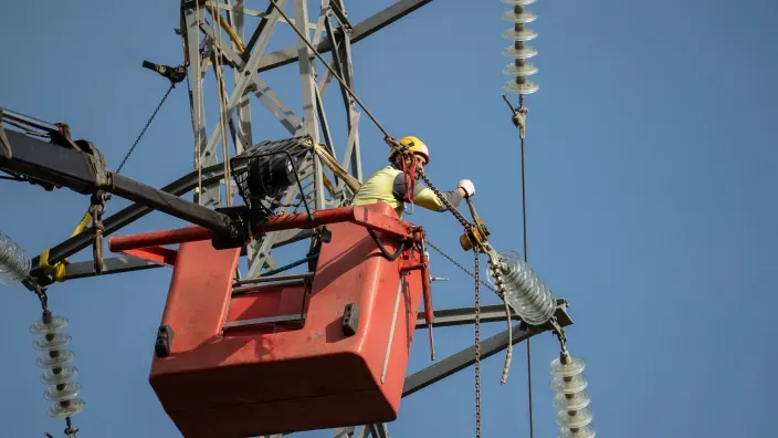 Operario realizando labores de mantenimiento en una torre de alta tensión desde una plataforma elevadora.