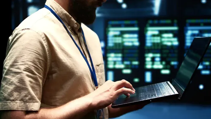 Técnico trabajando con un portátil frente a racks de servidores en un centro de datos.