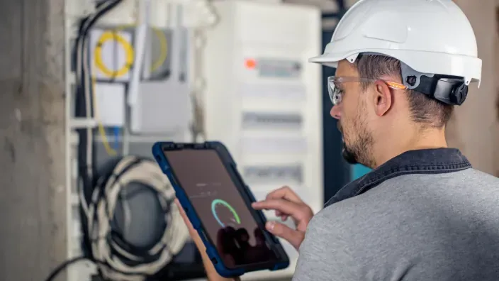 Técnico con casco revisando una instalación eléctrica o de gas con una tablet.