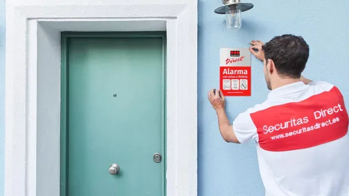 écnico de Securitas Direct colocando un cartel de alarma en la fachada de una vivienda.