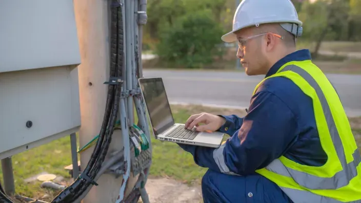 Técnico de telecomunicaciones usando un portátil para el despliegue de redes de fibra óptica en exteriores.