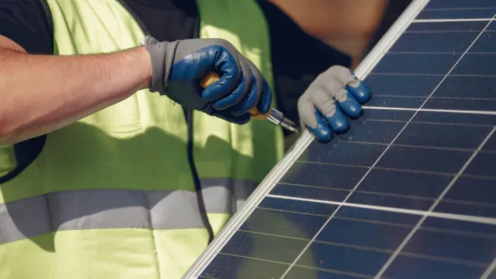 Técnico instalando un panel solar fotovoltaico con herramientas y guantes de seguridad