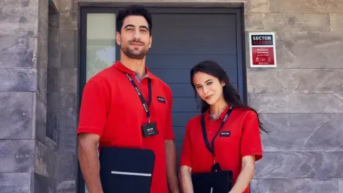 Técnicos instaladores de Sector Alarm uniformados de rojo frente a una vivienda protegida.
