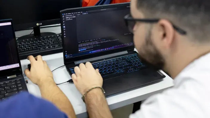 Dos técnicos trabajando juntos en ordenadores portátiles mientras revisan y programan código.