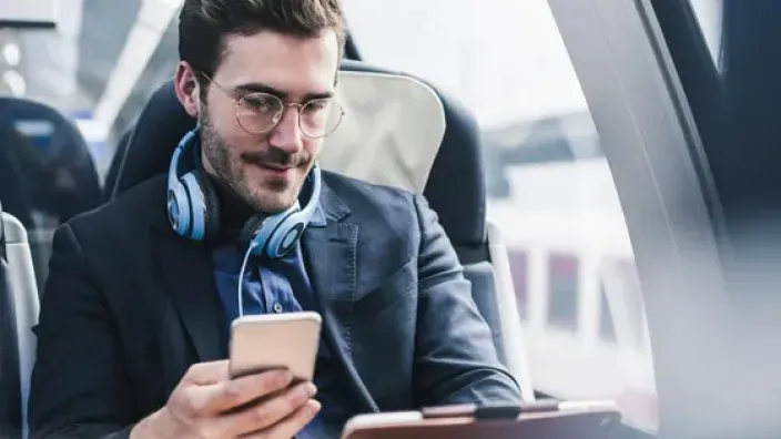 Joven profesional con gafas usando su smartphone para trabajar o ver contenido multimedia mientras viaja en tren.
