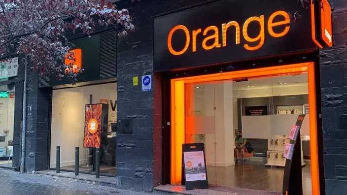 Fachada de una tienda Orange con el logotipo iluminado en color naranja.