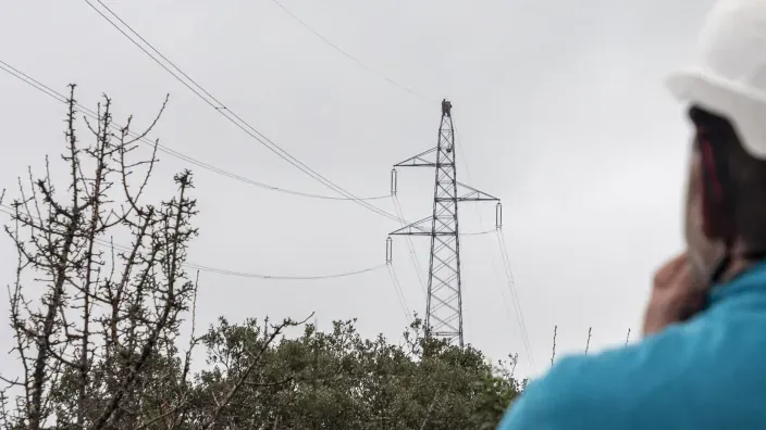 Torre de alta tensión con líneas eléctricas en zona rural vista desde el suelo.
