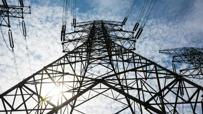 Torre de alta tensión contra el cielo azul con cables eléctricos en primer plano