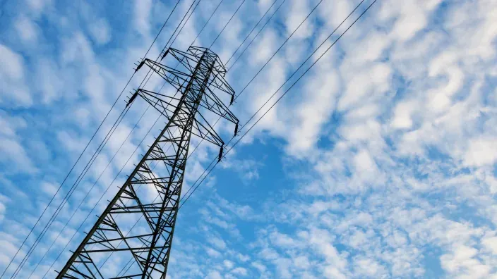 Torre eléctrica de alta tensión con cables y cielo azul despejado al fondo.