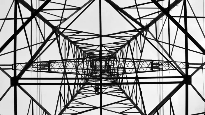 Estructura metálica de una torre eléctrica vista desde abajo con entramado de vigas y cables.