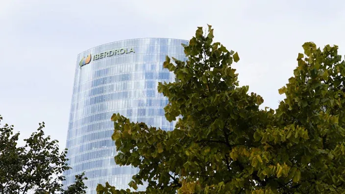 Torre Iberdrola, sede central de la compañía eléctrica en Bilbao, con su logo visible entre las hojas de un árbol en primer plano.