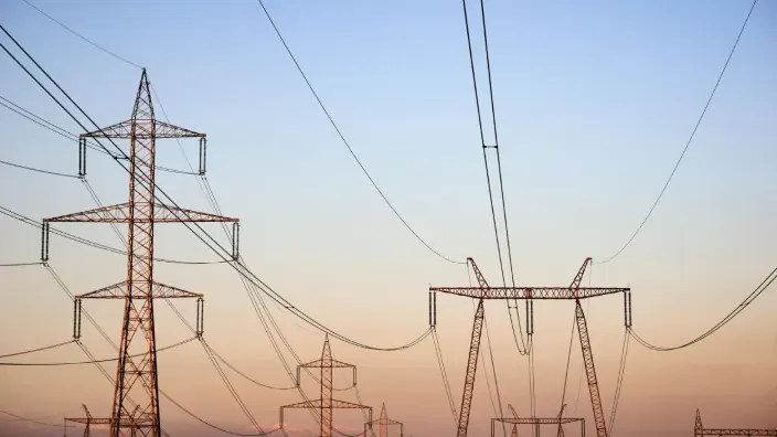 Torres de alta tensión y líneas eléctricas sobre el horizonte al atardecer.