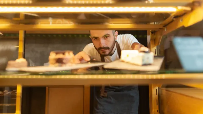 Trabajador colocando pasteles en una vitrina refrigerada.