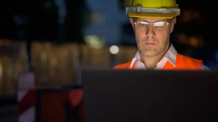 Ingeniero con casco y chaleco reflectante usando un portátil ante un ciberataque.