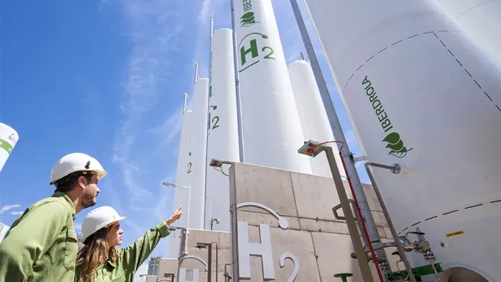 Dos trabajadores con casco junto a depósitos de hidrógeno con la marca Iberdrola
