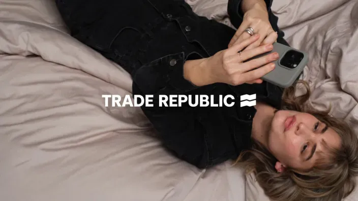 Mujer joven tumbada en la cama usando la app de inversión de Trade Republic en su móvil.