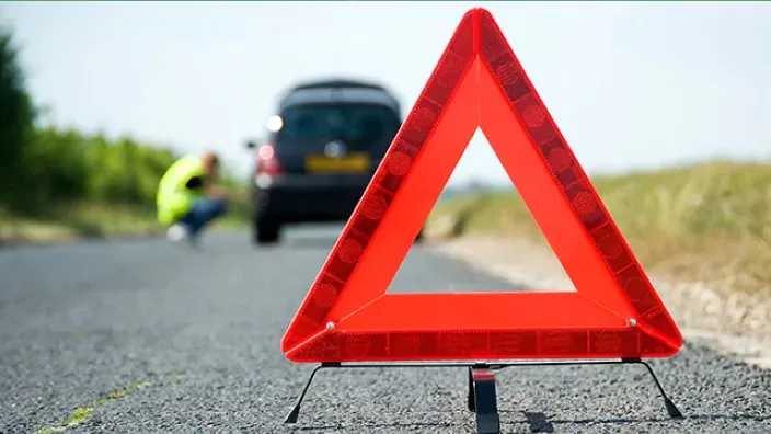 Un triangulo de emergencia colocado en el asfalto con un coche averiado al fondo