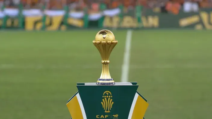 El trofeo de la Copa de África de Naciones sobre un pedestal en el césped de un estadio de fútbol antes de la final.