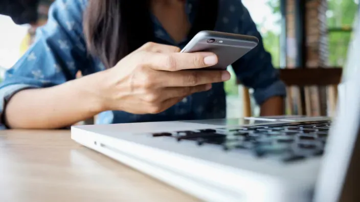 Persona usando un smartphone y un portátil para realizar gestiones de banca digital y administración online.